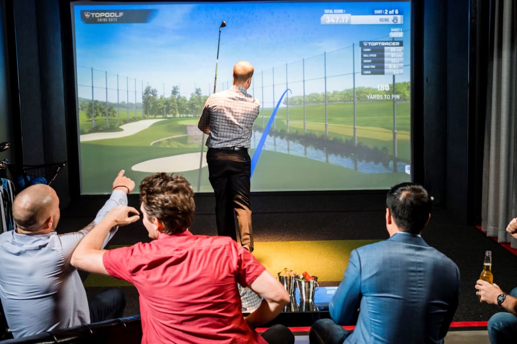 Men playing virtual golf in a simulator room with a large screen and golf clubs in Atlanta, Georgia.