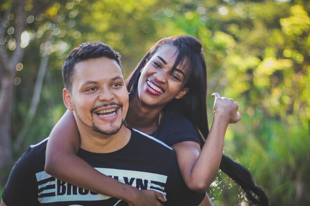 A joyful couple shares a playful piggyback ride in a lush, green forest setting in Atlanta, Georgia.