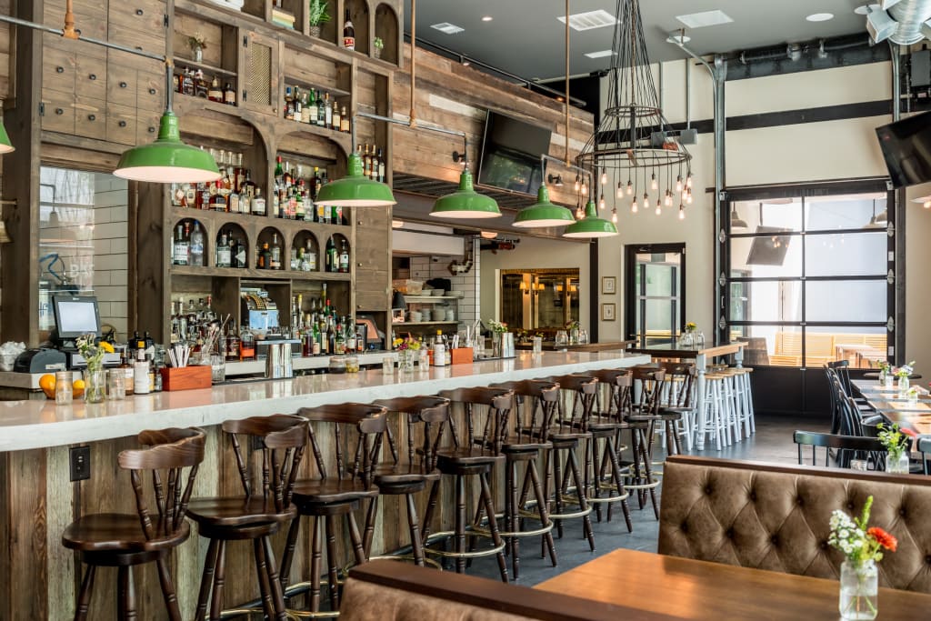 A rustic bar with wooden decor, green pendant lights, and a long counter with stools in Atlanta, Georgia.