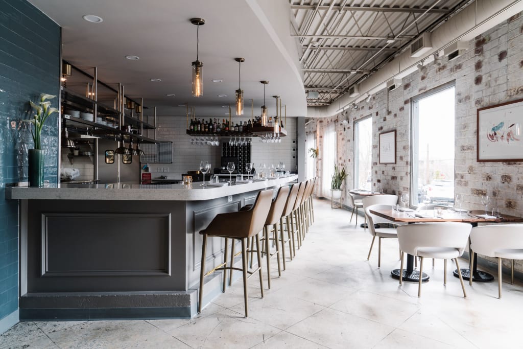 Modern restaurant interior with a long bar, high stools, and tables near large windows in Atlanta, Georgia.