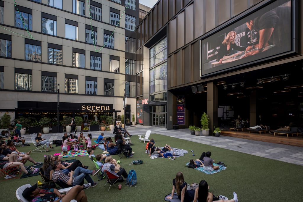 People relax on a grassy rooftop patio with a large screen showing a movie in Atlanta, Georgia.
