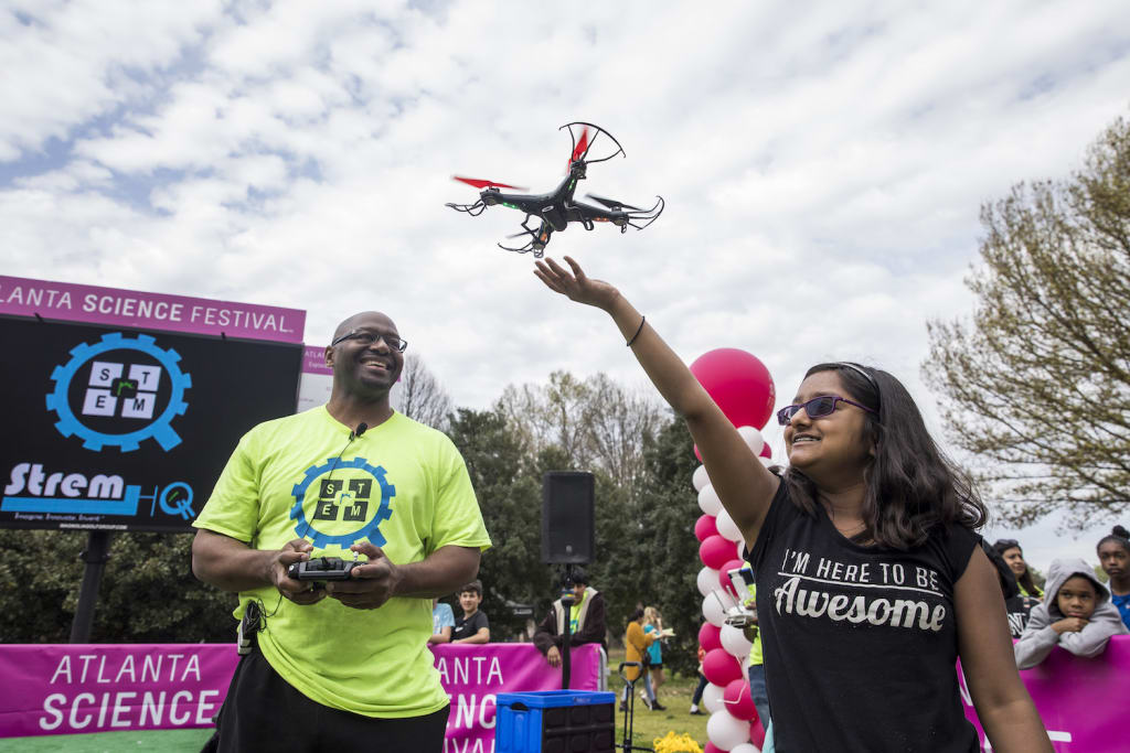Two people at a science festival control a drone flying overhead in Atlanta, Georgia.