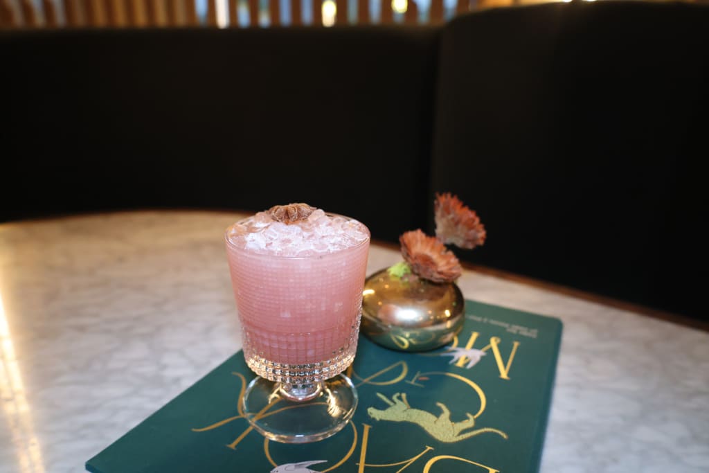A pink cocktail garnished with a flower sits on a green book with gold lettering in Atlanta, Georgia.