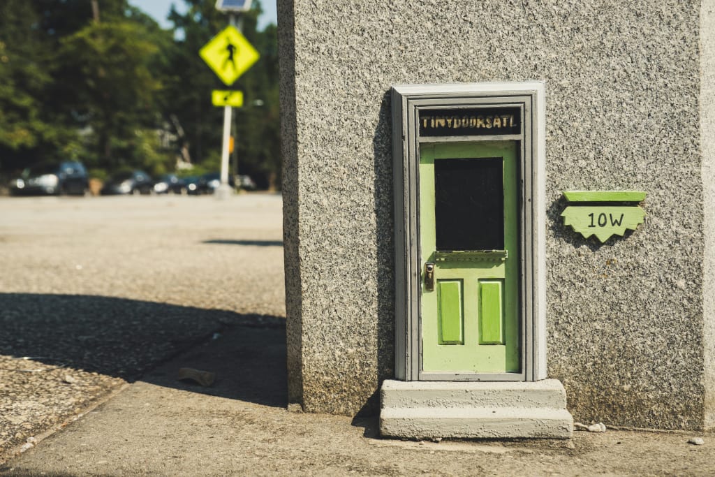Tiny green door with 'Tiny Bookshop' sign on concrete wall in parking lot in Atlanta, Georgia.