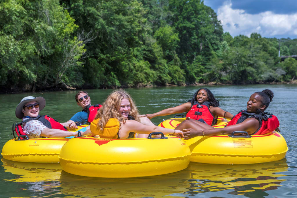 Four people enjoying a sunny day on yellow inner tubes in a river surrounded by trees in Atlanta, Georgia.