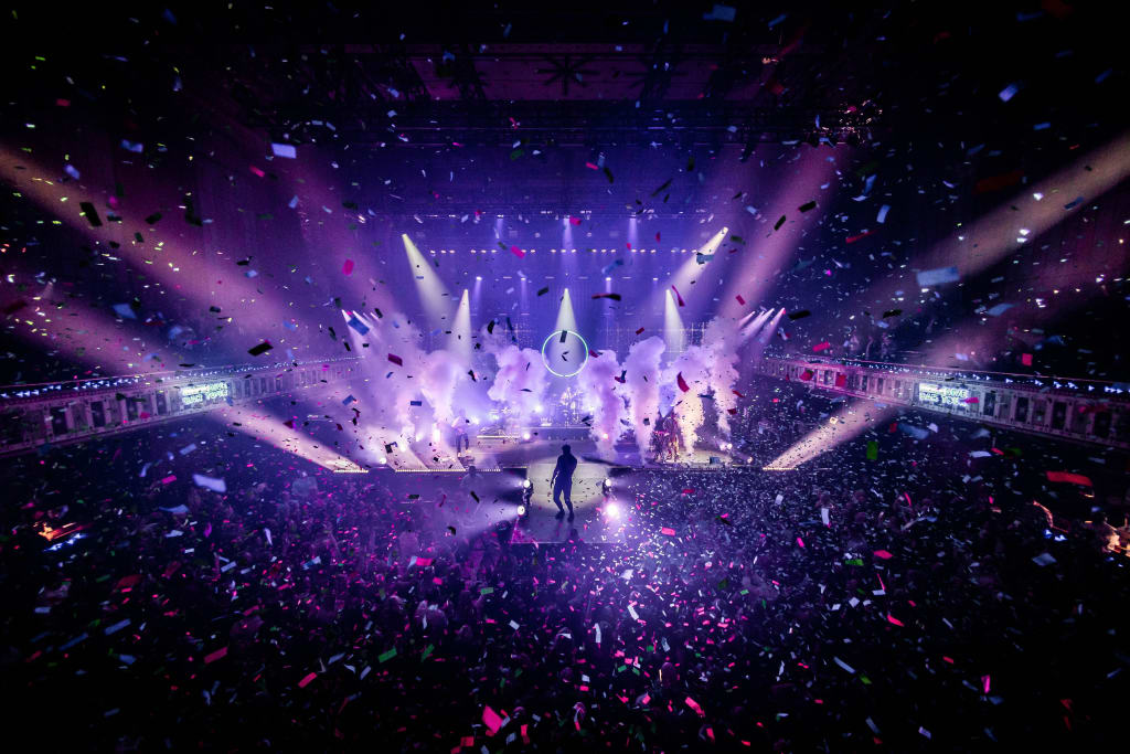 A vibrant concert scene with a performer on stage, surrounded by colorful lights and confetti in Atlanta, Georgia.
