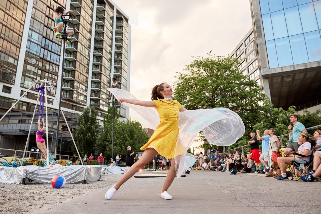 A woman in a yellow dress dances with a flowing white cloth in an outdoor urban performance space in Atlanta, Georgia.