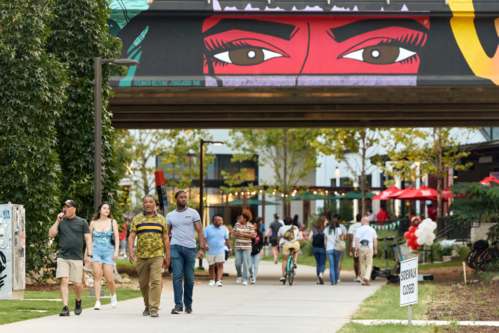 A diverse group of people walks along a tree-lined path under a colorful mural in Atlanta, Georgia.