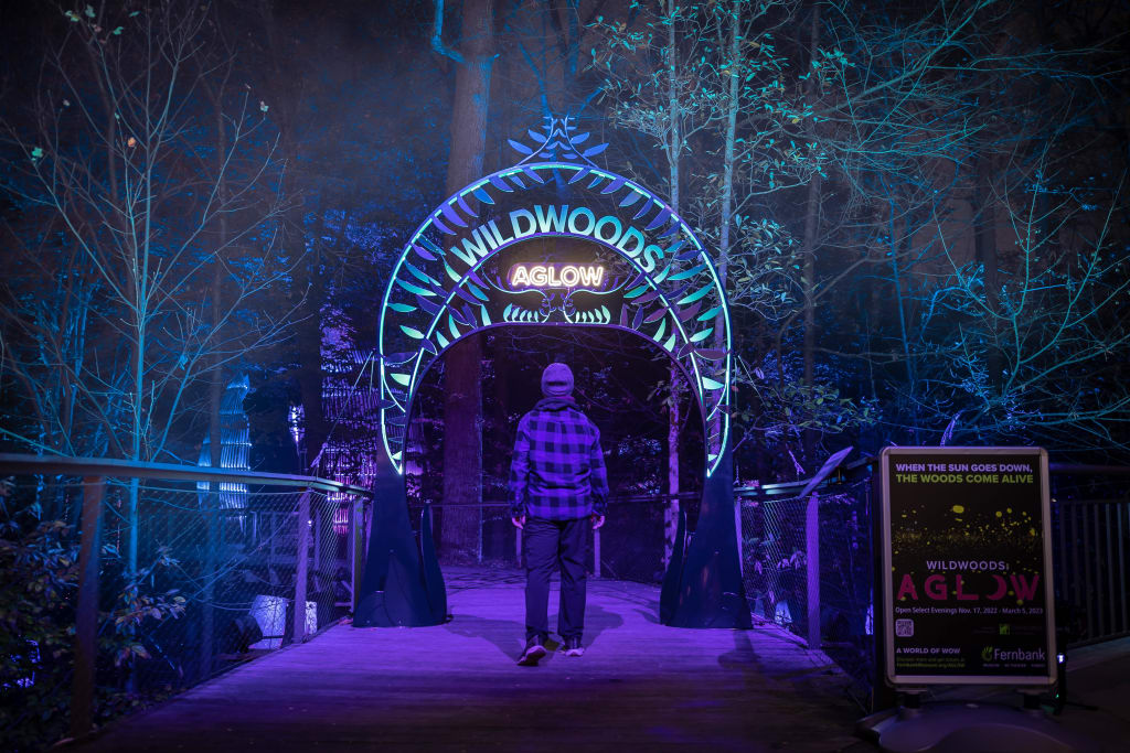 A person walks through a glowing archway into a forest illuminated by blue lights in Atlanta, Georgia.