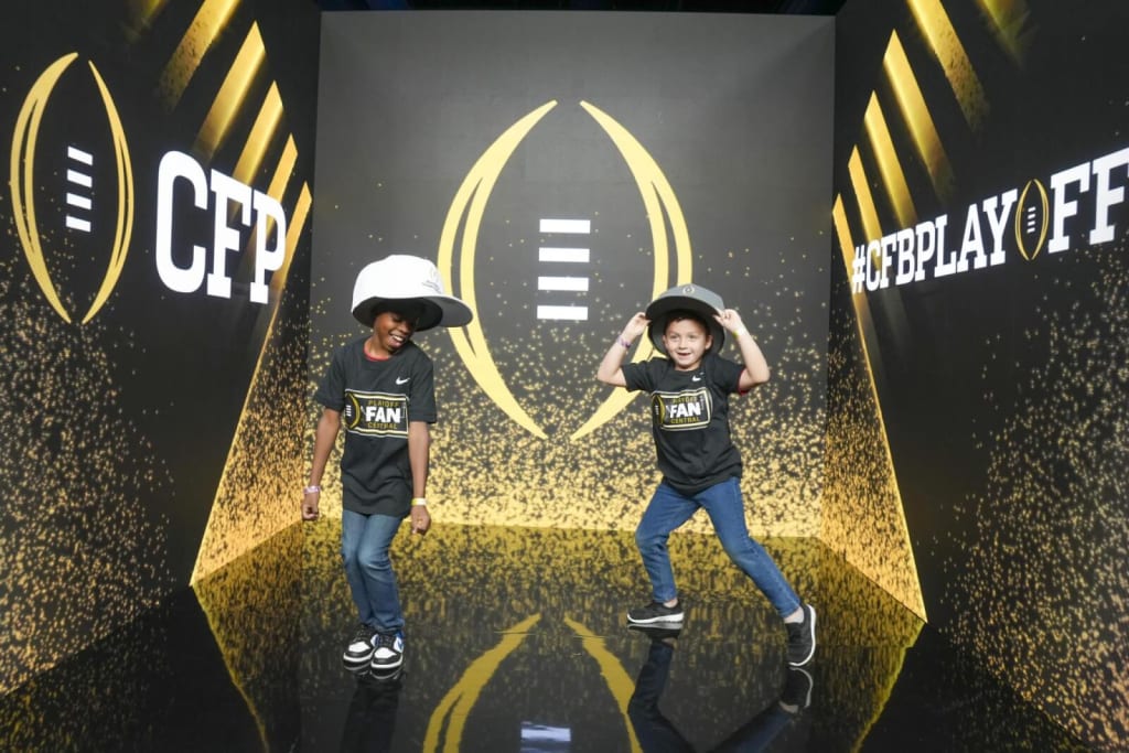 Two children in football fan gear pose in front of a College Football Playoff backdrop in Atlanta, Georgia.