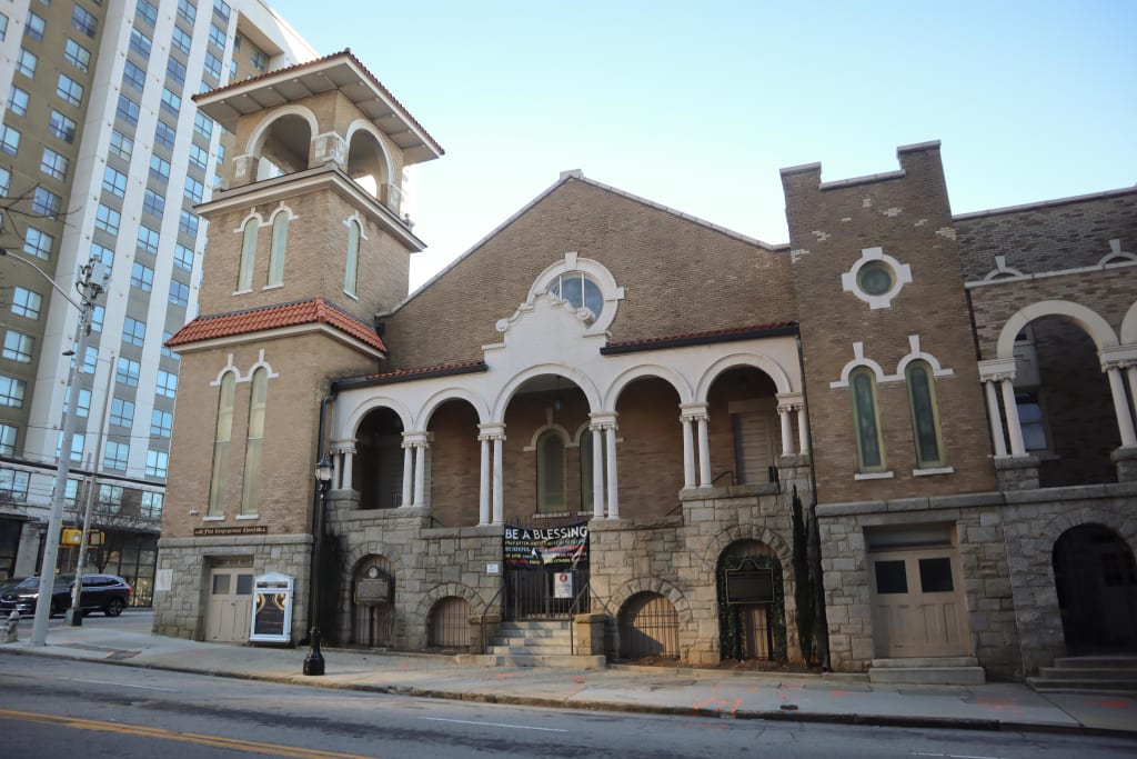 A historic church with a bell tower and arched windows stands beside a modern high-rise in Atlanta, Georgia.