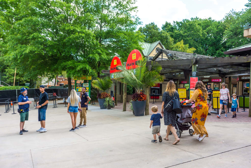 A family walks through a zoo entrance with colorful signs and lush greenery in Atlanta, Georgia.