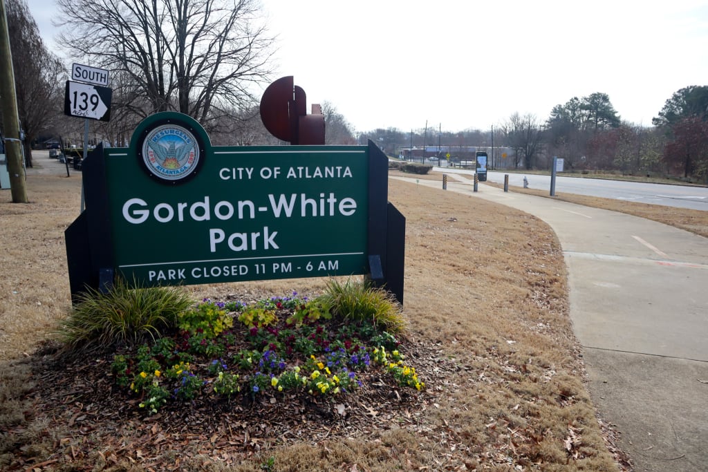 Explore Atlanta Beltline Southwest Trail 4 A green sign with a seal marks the entrance to Gordon-White Park in Atlanta, surrounded by flowers in Atlanta, Georgia.
