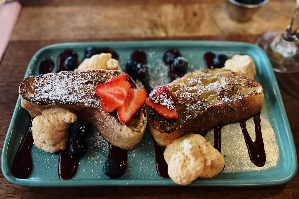 A plate of French toast topped with strawberries, blueberries, and whipped cream, drizzled with syrup in Atlanta, Georgia.