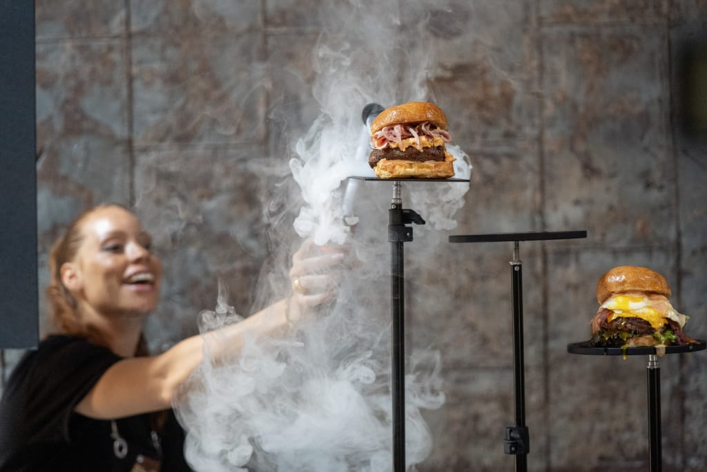 A woman uses dry ice to create smoke effects around three mouthwatering burgers on stands in Atlanta, Georgia.