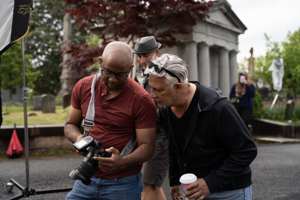 Two men examine a camera in a cemetery with a classical building in the background in Atlanta, Georgia.