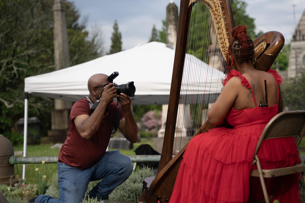 A photographer captures a musician playing a harp in a garden setting in Atlanta, Georgia.