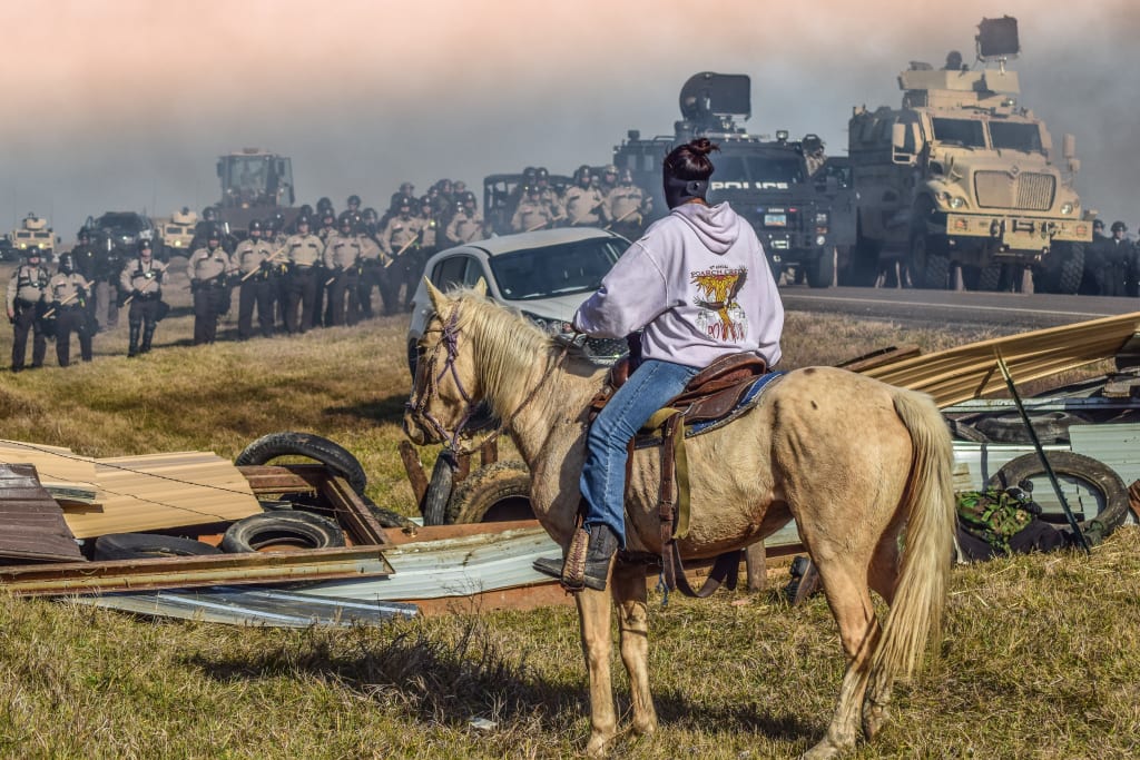 A person on horseback observes a tense standoff between police and protesters on a rural road in Atlanta, Georgia.