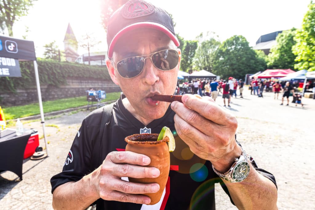 A man in a black cap and sunglasses drinks from a clay cup with a lime wedge at an outdoor event in Atlanta, Georgia.