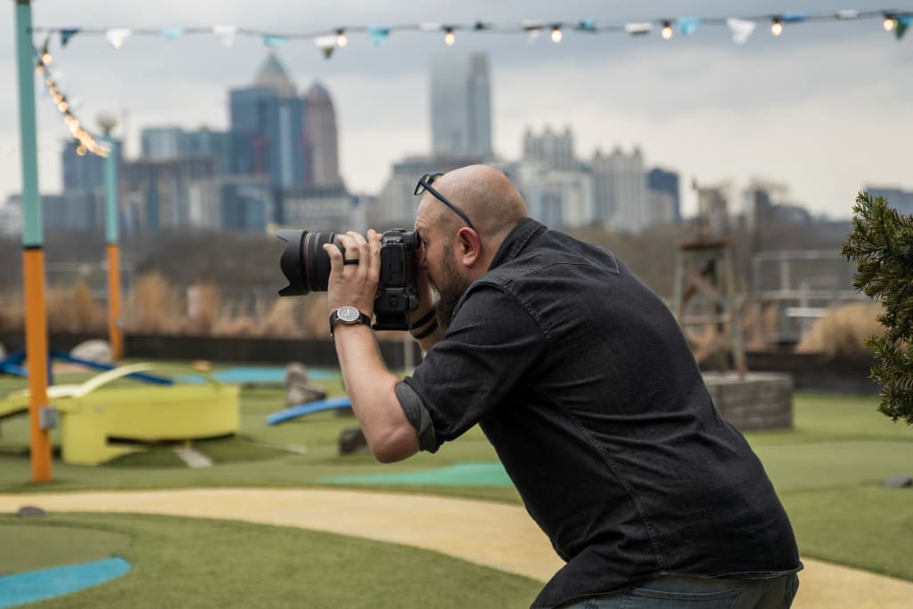 A bald man with glasses and a watch is taking a photograph of the city skyline in Atlanta, Georgia.