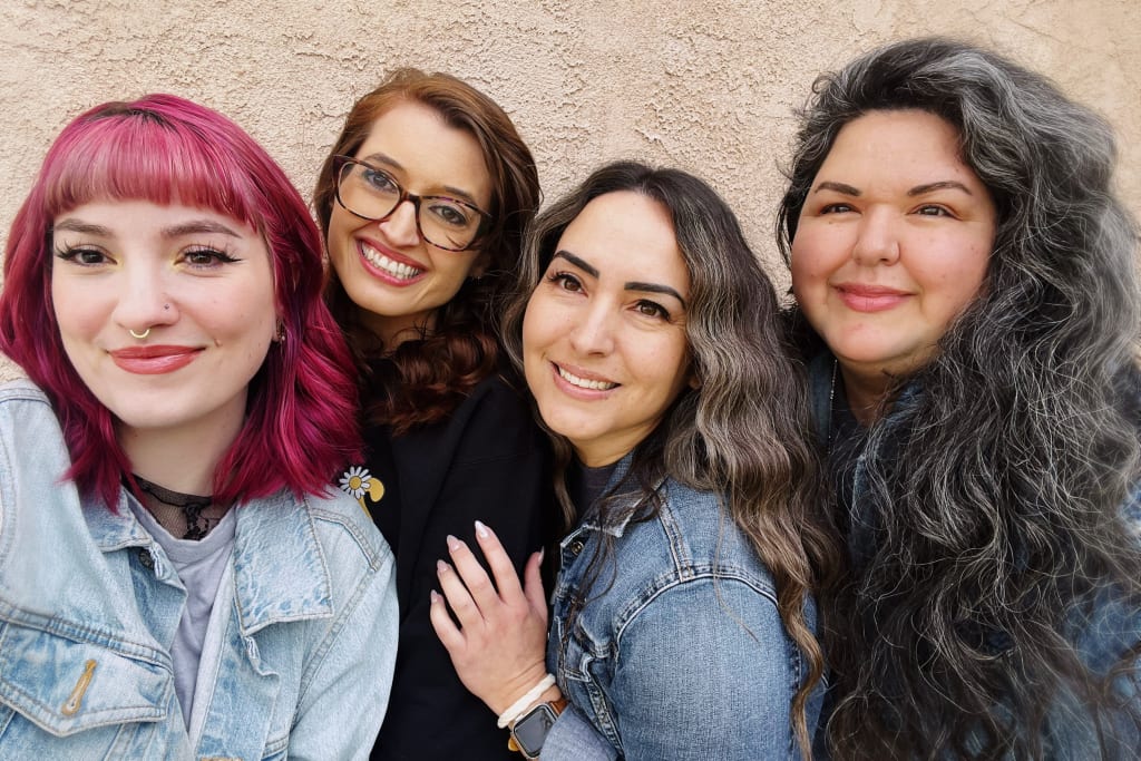 Four women with colorful hair and smiles pose together against a textured wall in Atlanta, Georgia.