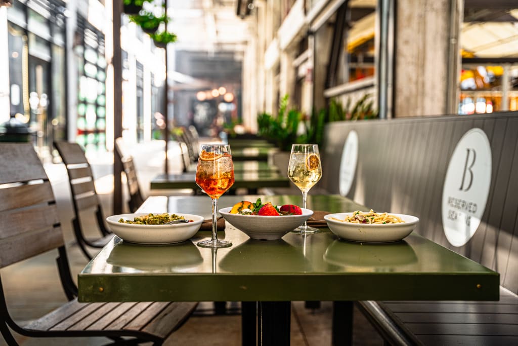 Outdoor restaurant patio with wooden chairs, green table, and colorful food and drinks in Atlanta, Georgia.