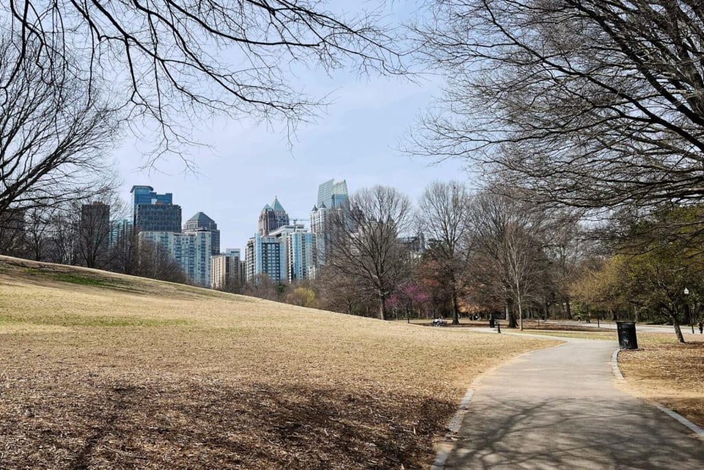 A winding path through a park with bare trees leads towards a city skyline in Atlanta, Georgia.