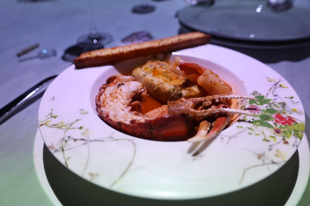A beautifully presented seafood dish with lobster tail, shrimp, and a rich red sauce on a floral plate in Atlanta, Georgia.