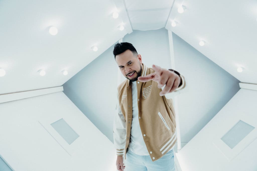 A man in a beige varsity jacket points confidently in a modern, white room in Atlanta, Georgia.