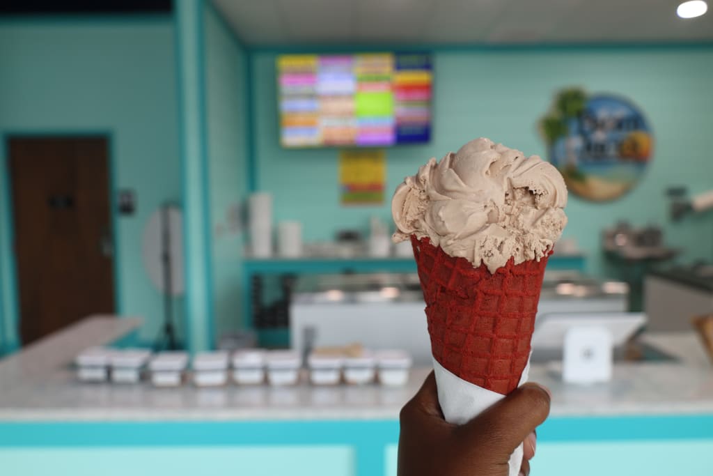 A hand holds a red waffle cone filled with chocolate ice cream in a bright ice cream shop in Atlanta, Georgia.