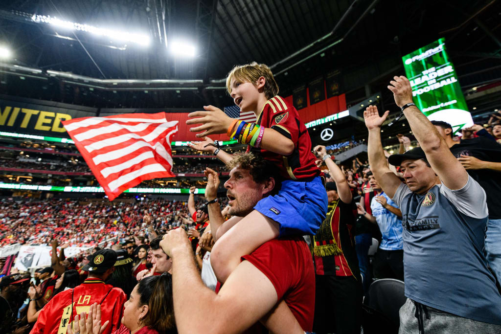 A young boy rides on a man's shoulders, waving an American flag at a crowded stadium event in Atlanta, Georgia.