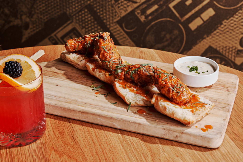 A wooden board holds chicken wings with a creamy dipping sauce and a glass of red drink with an orange slice in Atlanta, Georgia.