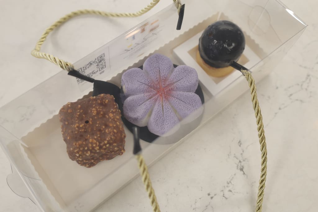 Three gourmet desserts in a clear plastic box with gold rope handles in Atlanta, Georgia.