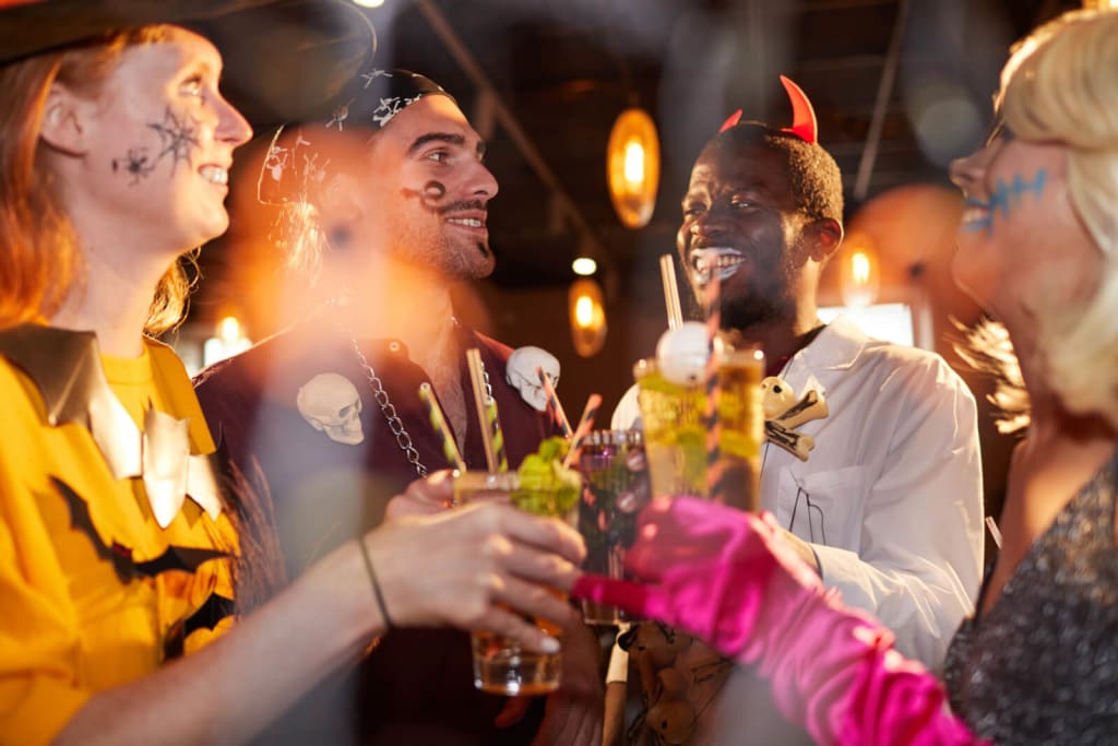 Four people in Halloween costumes raise their drinks in a toast at a festive party in Atlanta, Georgia.