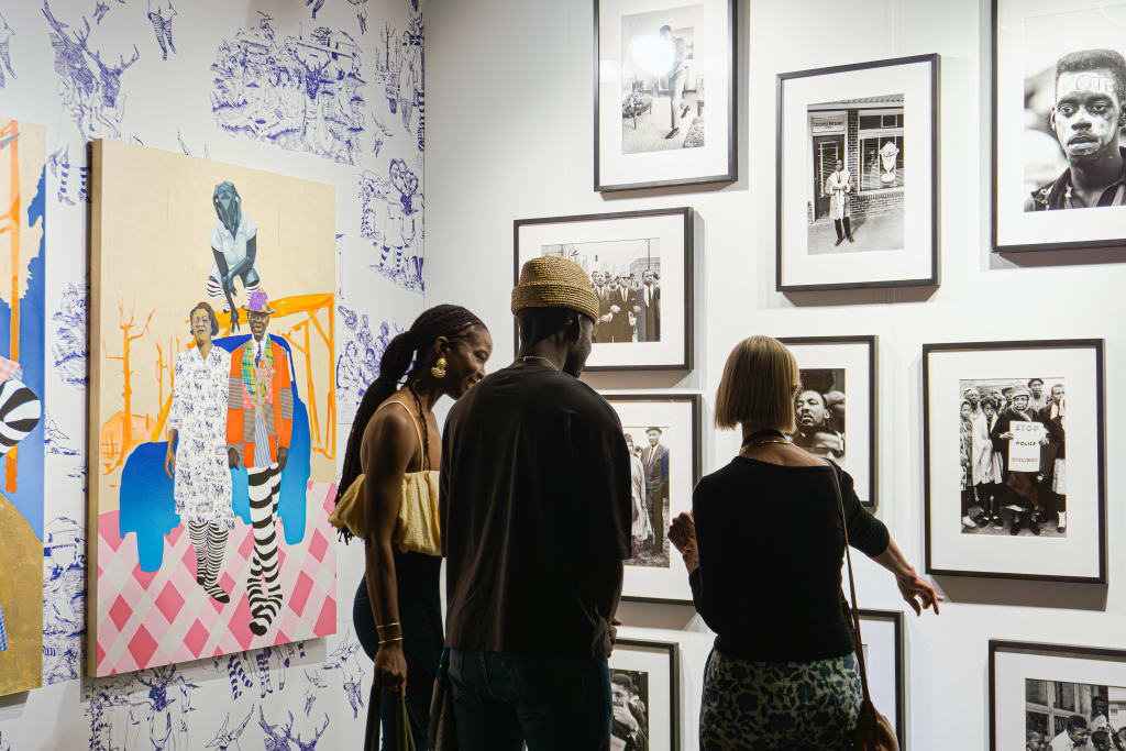 Ultimate Guide to Atlanta Art Fair 2025 1 Three people examine framed photographs and artwork in a gallery setting in Atlanta, Georgia.