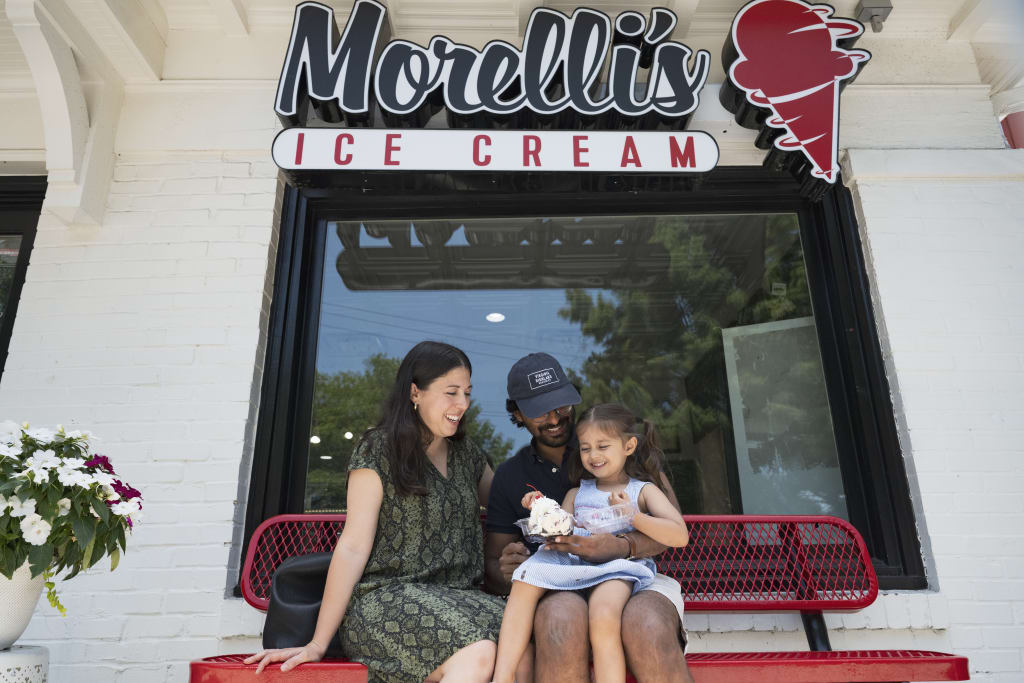 A family of three enjoys ice cream on a bench outside Morelli's Ice Cream shop in Atlanta, Georgia.