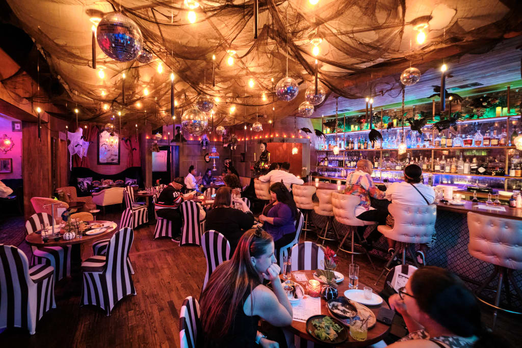 A dimly lit restaurant with a spooky Halloween theme, featuring black and white striped chairs, hanging disco balls, and a bar with glowing bottles in Atlanta, Georgia.