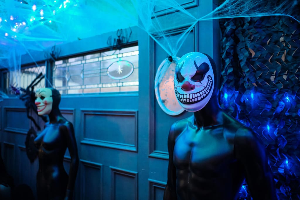 Grown-Up Guide to Halloween in Atlanta 2 Two mannequins, one with a clown mask and another with a cat mask, stand in a dimly lit room decorated with blue lights and spiderwebs in Atlanta, Georgia.