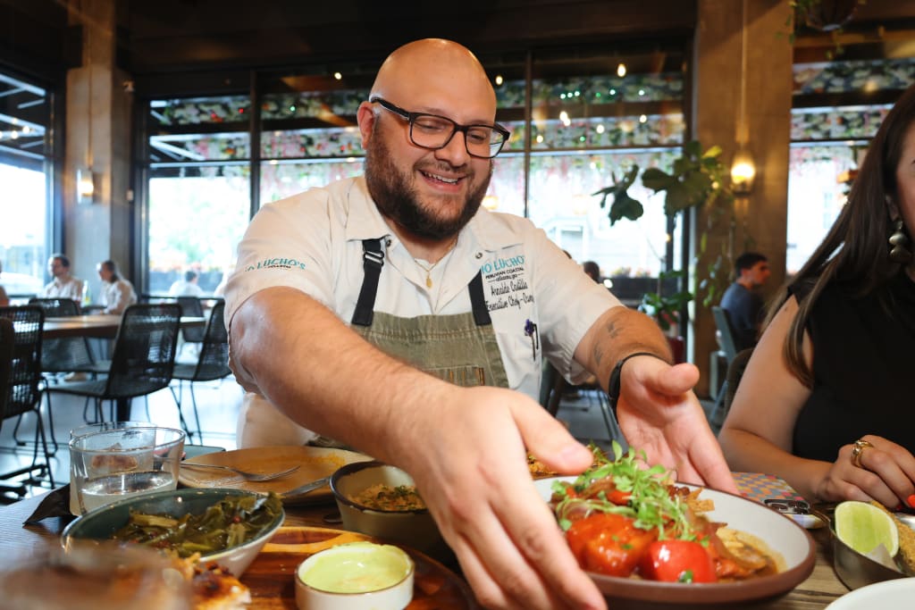 A smiling chef in a restaurant kitchen serves a colorful dish to a guest at a table in Atlanta, Georgia.