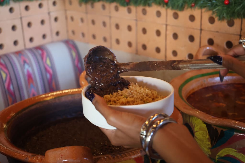 A hand pours dark sauce over rice in a white bowl, held over colorful ceramic pots in Atlanta, Georgia.