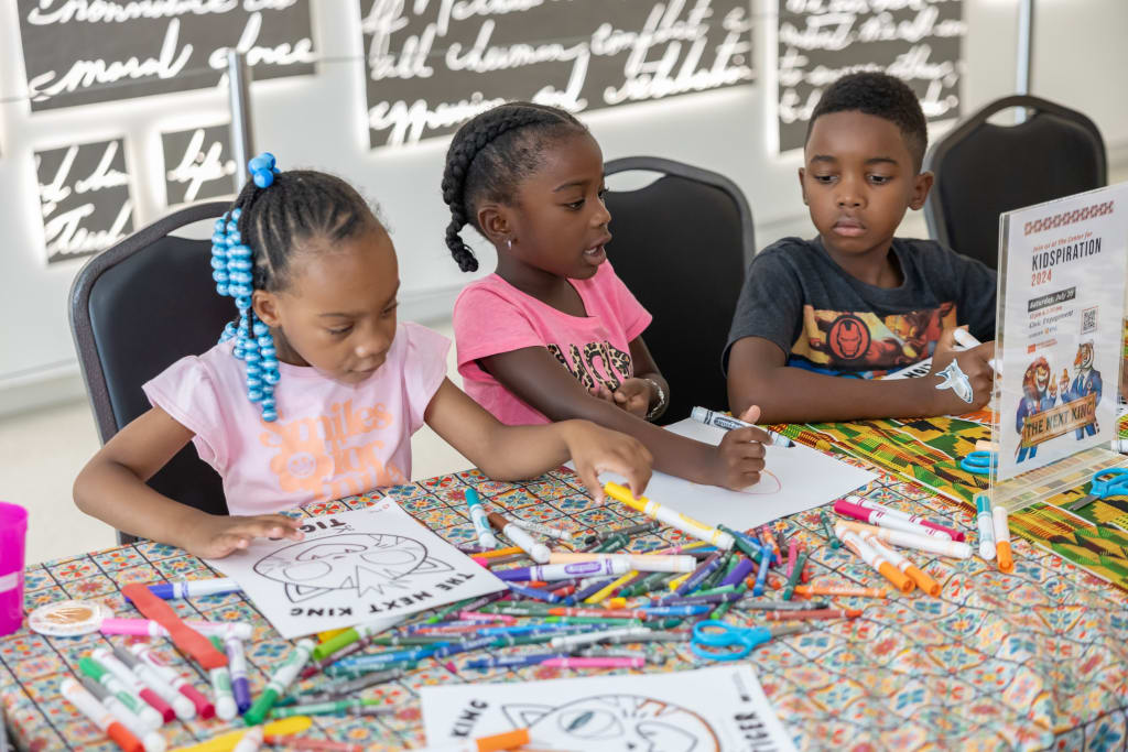 Three children are engaged in coloring activities at a table with various art supplies in Atlanta, Georgia.