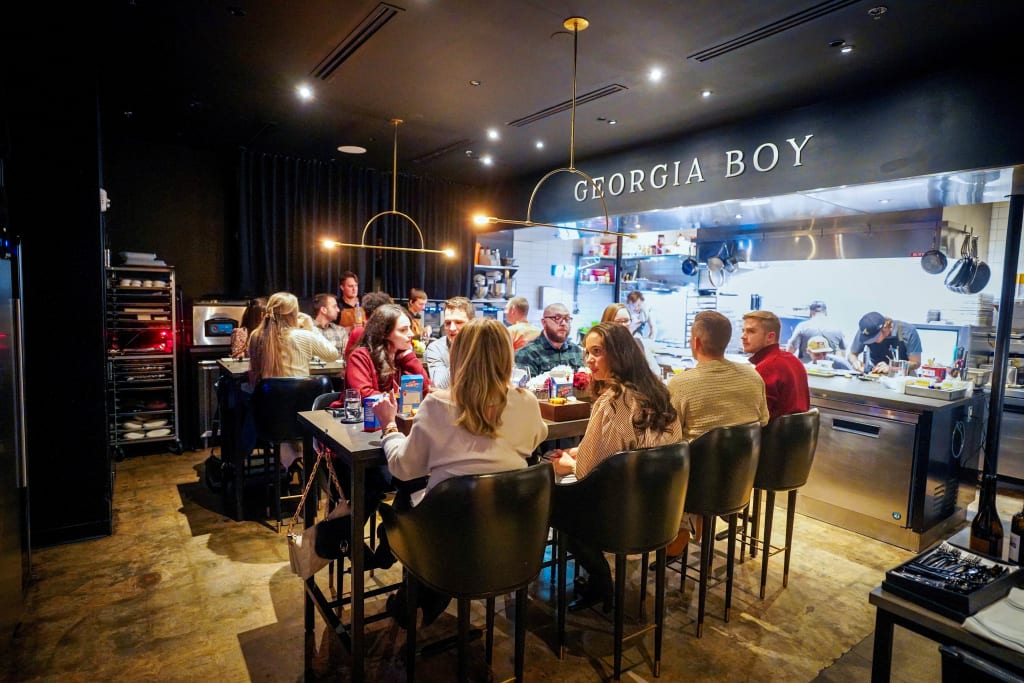 Patrons enjoy a lively meal at a modern restaurant with an open kitchen in Atlanta, Georgia.