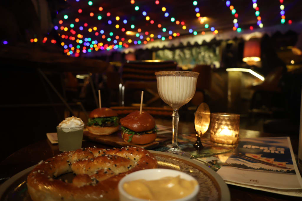 A cozy restaurant table setting with burgers, pretzel, and colorful string lights overhead in Atlanta, Georgia.