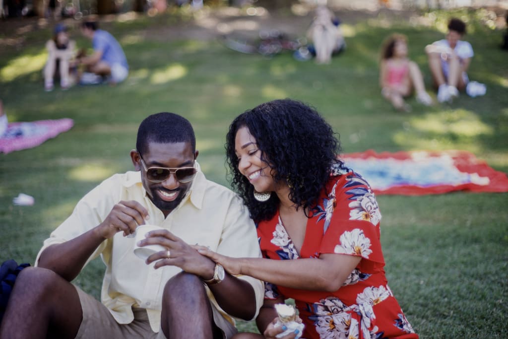 A couple enjoys a sunny day in the park, sharing a moment of laughter and intimacy while eating ice cream in Atlanta, Georgia.