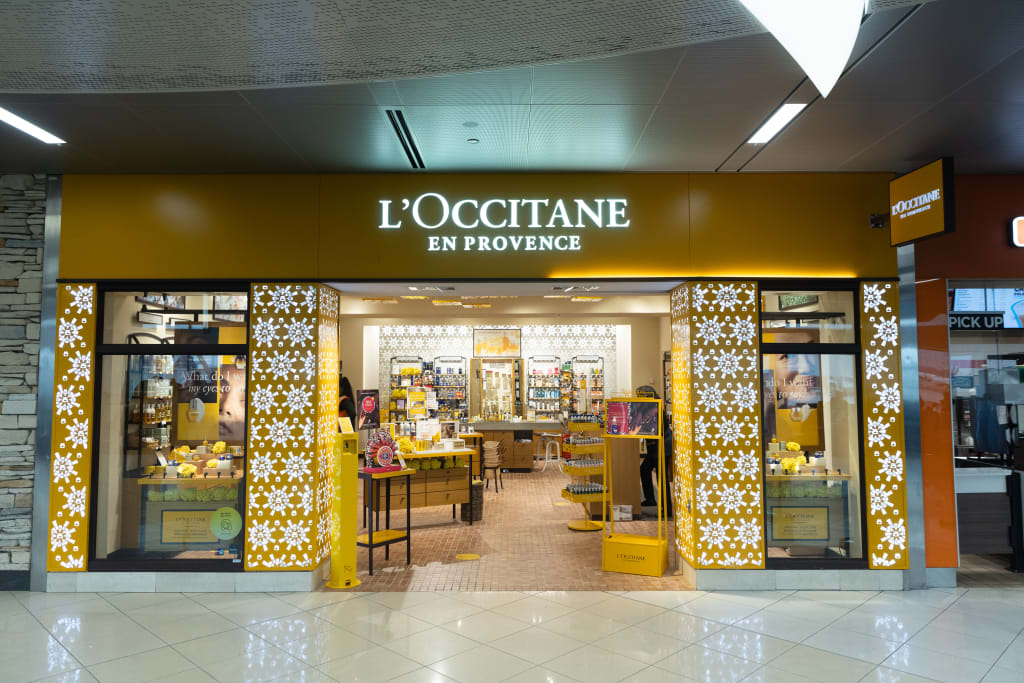 A brightly lit L'Occitane en Provence store with a yellow facade and intricate white latticework on the windows, showcasing a variety of beauty products inside in Atlanta, Georgia.