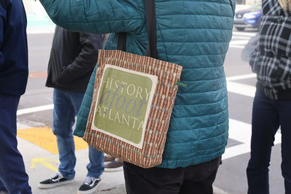 A person wearing a teal jacket carries a tote bag with 'History Afoot Atlanta' printed on it in Atlanta, Georgia.