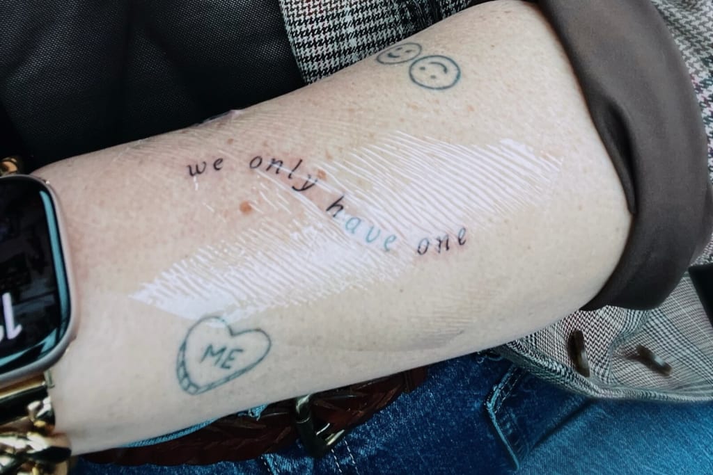 A person's arm with a tattoo reading 'we only have one' and other small tattoos, including a heart with 'ME' inside and two smiley faces in Atlanta, Georgia.