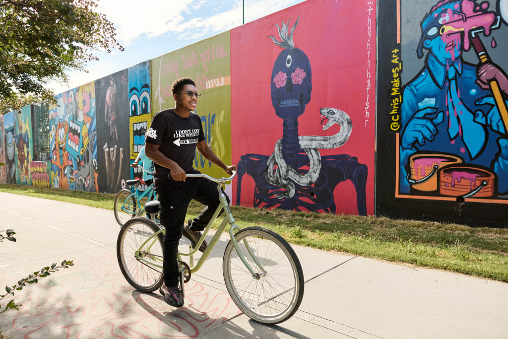 A young man rides a bicycle along a colorful mural-covered wall, enjoying a sunny day outdoors in Atlanta, Georgia.