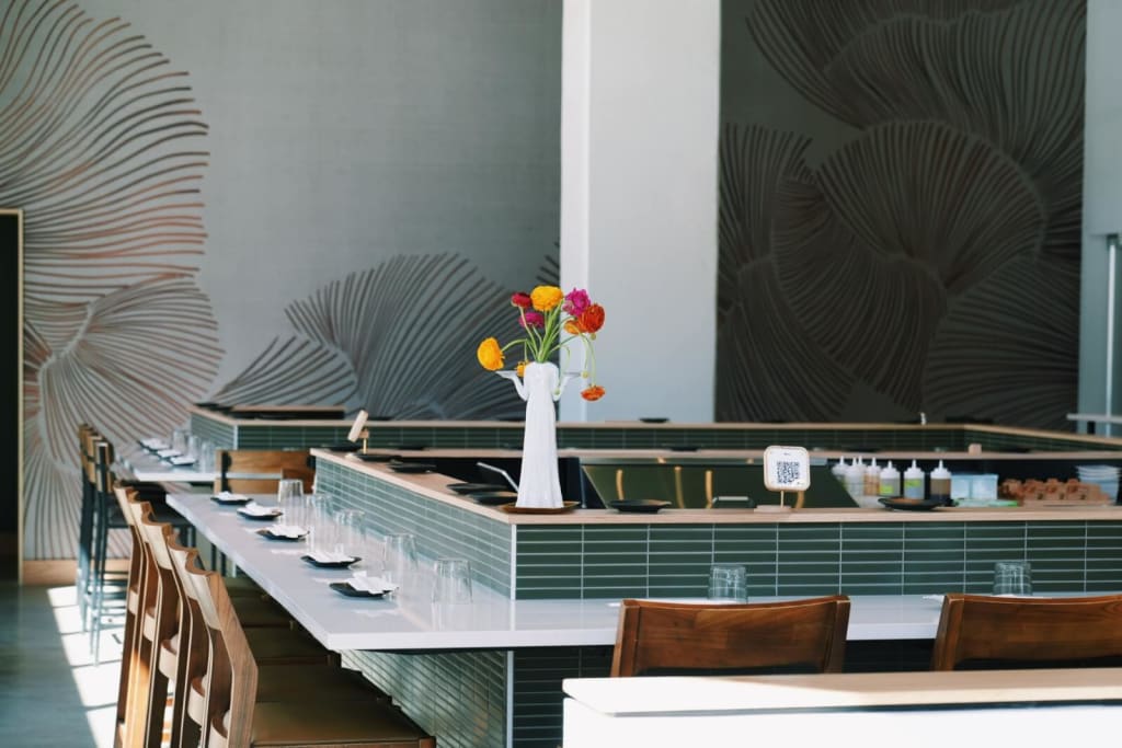 A modern restaurant interior with a long white counter, wooden chairs, and a vibrant floral arrangement on the bar in Atlanta, Georgia.