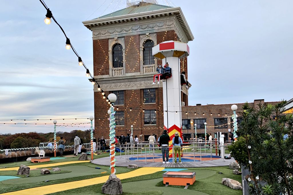 People play mini-golf on a rooftop course with a tall, lit tower in the background in Atlanta, Georgia.